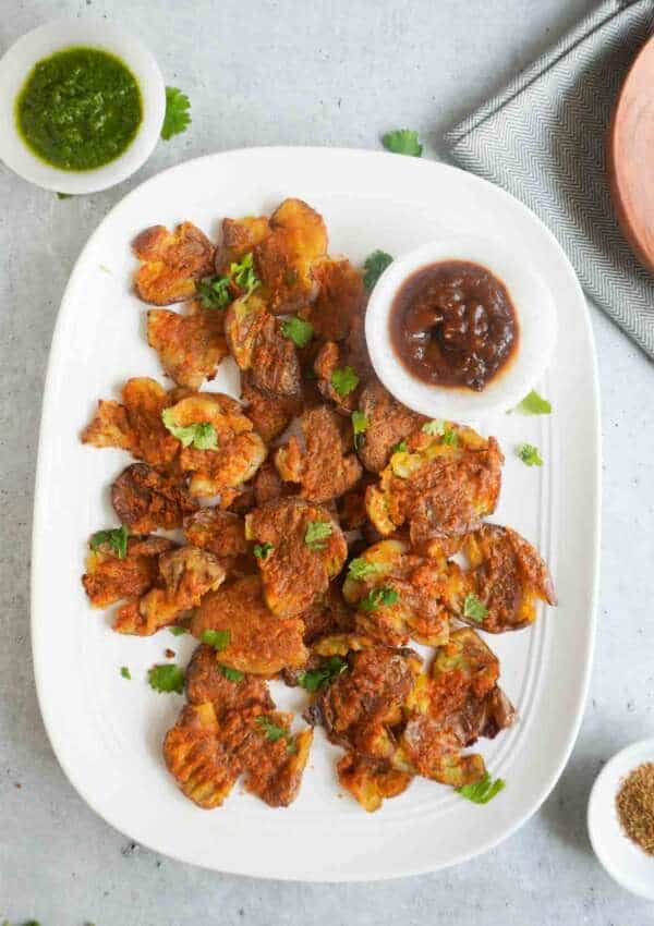 A platter with baked aloo pakoras and imli ki chutney and hari chutney in bowls