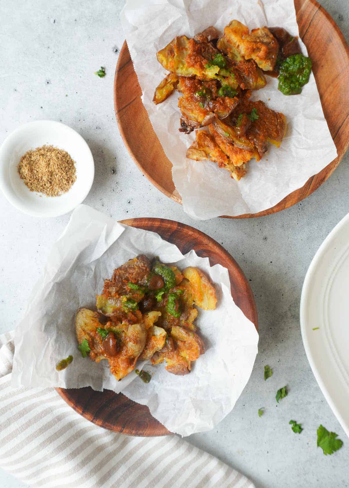 2 wooden bowls with healthy baked aloo pakoras on parchment with chutneys