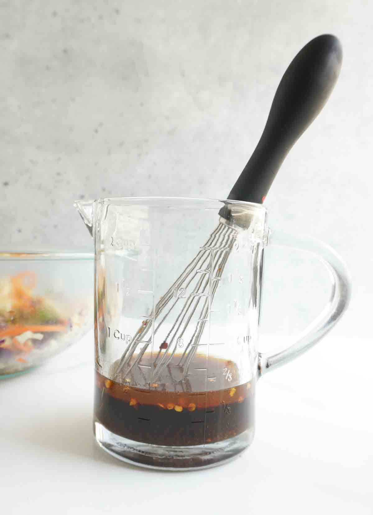 A small measuring jug and whisk with Thai dressing in it