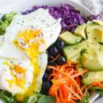 2 runny fried eggs on top of a bowl of vegetables
