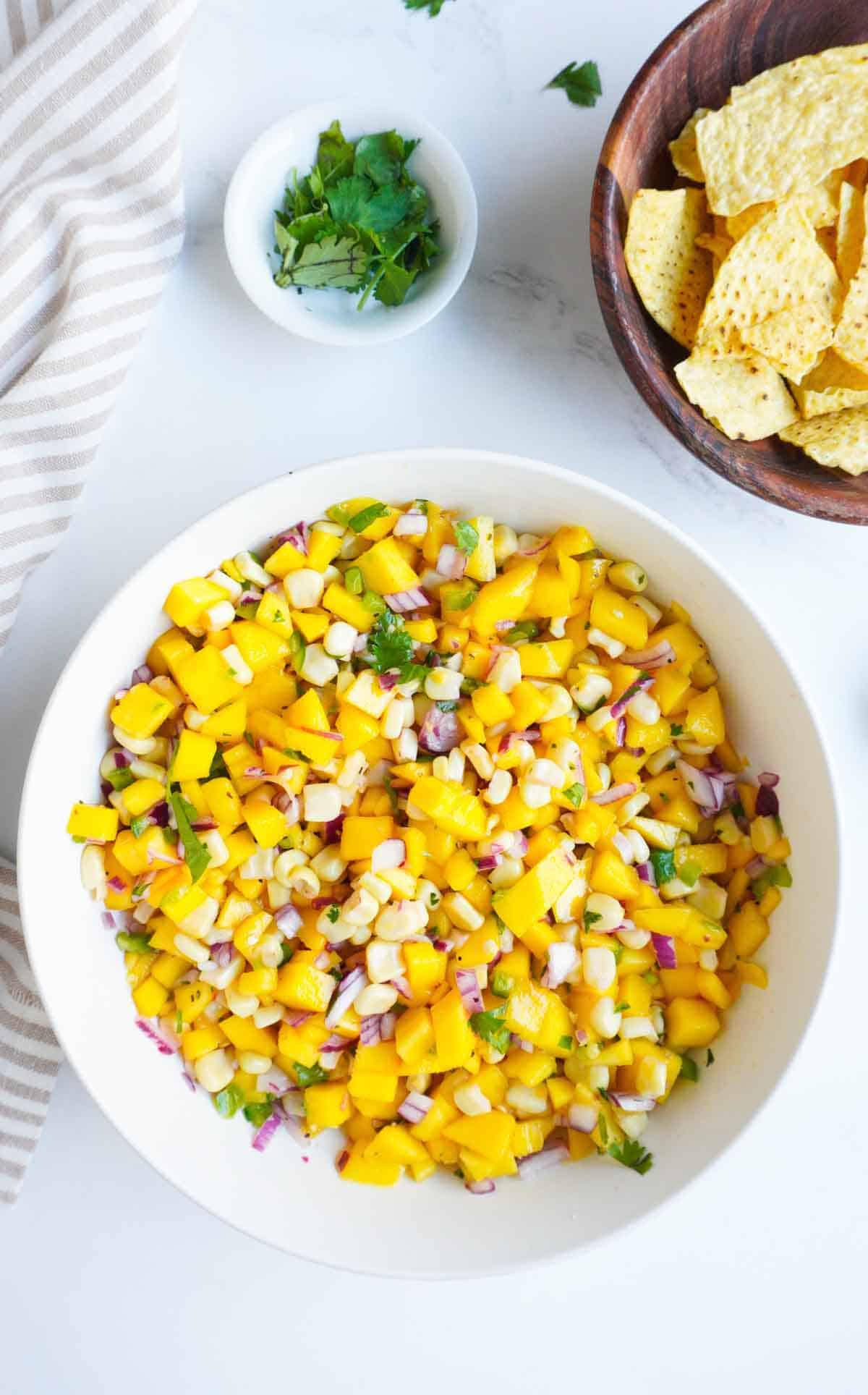 A bowl of mango corn salsa with a bowl of chips on the side.
