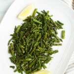 air fried asparagus in a platter with some lemon and crushed red pepper flakes in a bowl on the side.