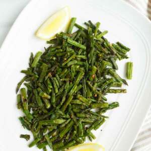 air fried asparagus in a platter with some lemon and crushed red pepper flakes in a bowl on the side.