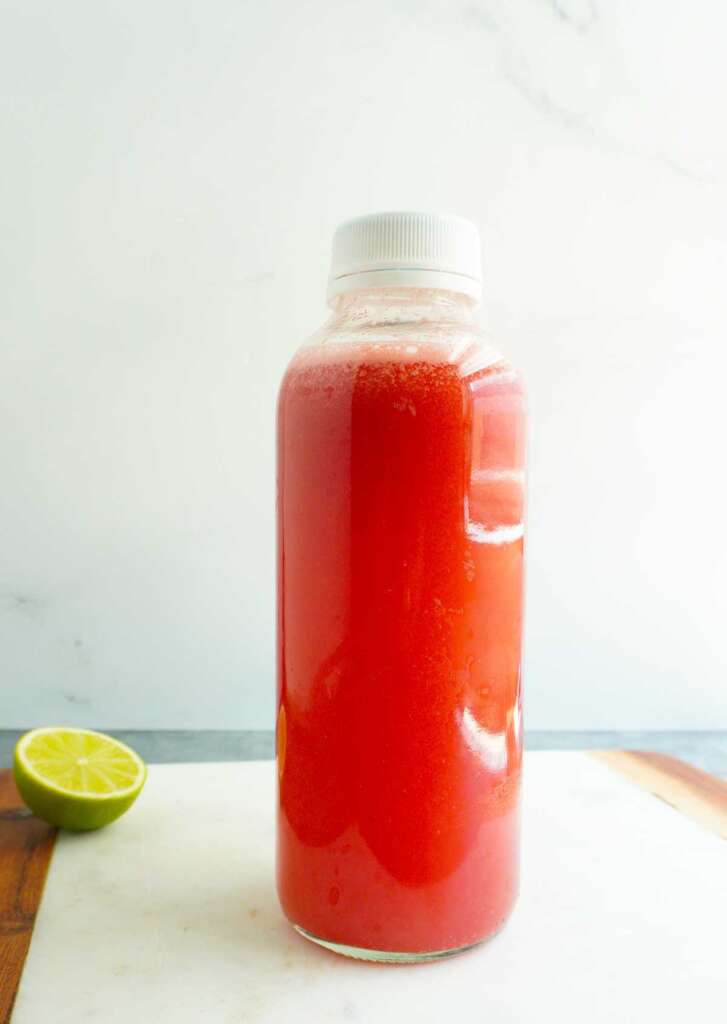 A clear glass bottle with watemelon juice.