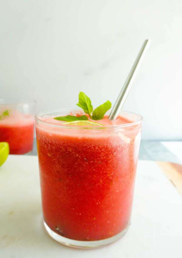a glass of watermelon juice with a straw and one in the background