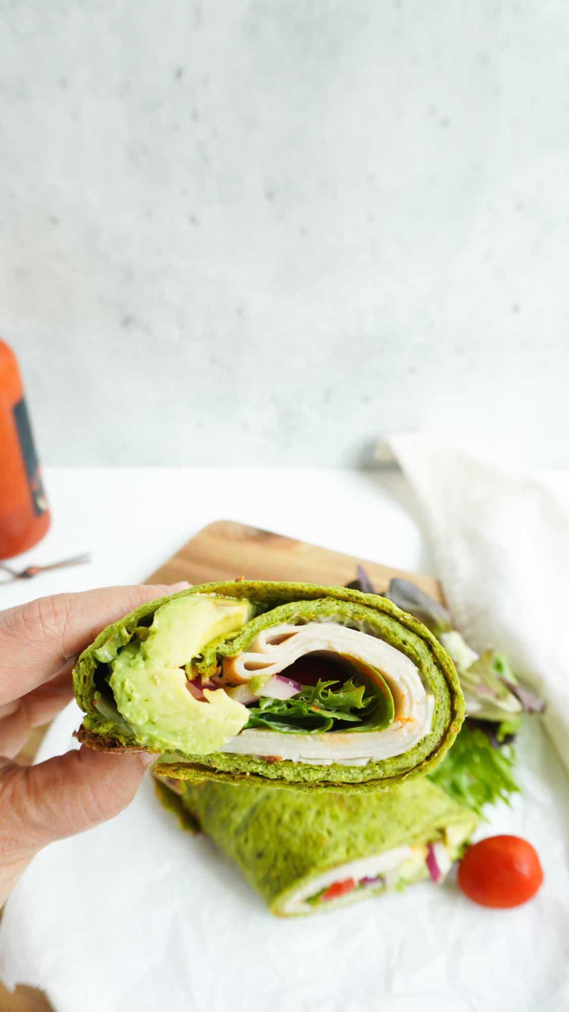a hand holding half a spinach cottage cheese wrap with a plate with the other half