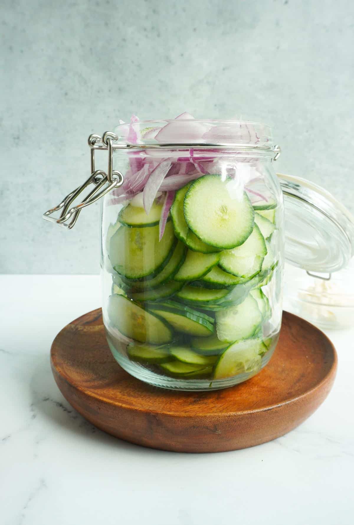 A glass jar with sliced cucumber and red onions