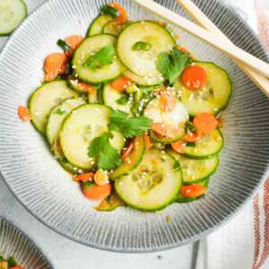A bowl of carrot cucumber salad with chop sticks propped on the edge