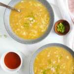 two bowls of Pakistani-style chicken corn soup with condiment bowls on the sides