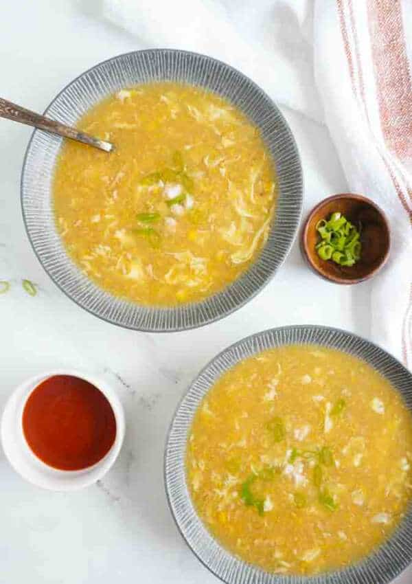 two bowls of Pakistani-style chicken corn soup with condiment bowls on the sides