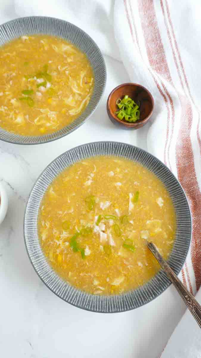 2 bowls of chicken corn soup with a wooden bowl with scallions on the side.