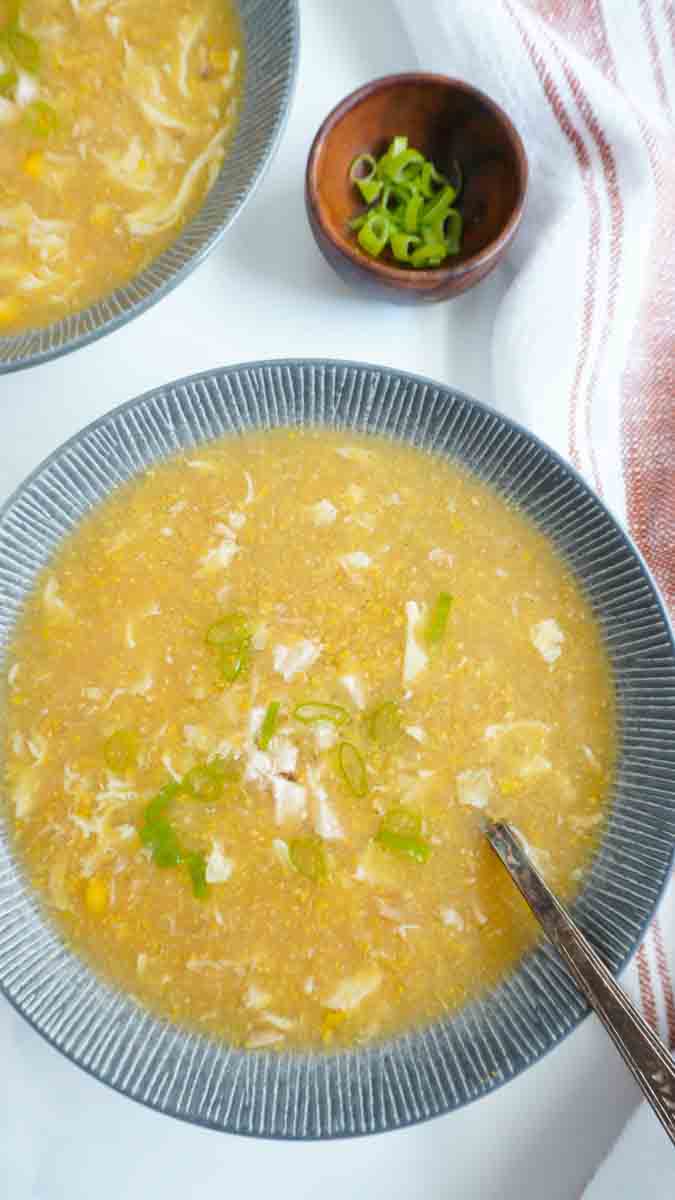 A bowl of chicken corn soup and another off to the side and a bowl of green onions 