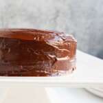 A frosted two layered almond flour chocolate cake on a white cake pedestal.
