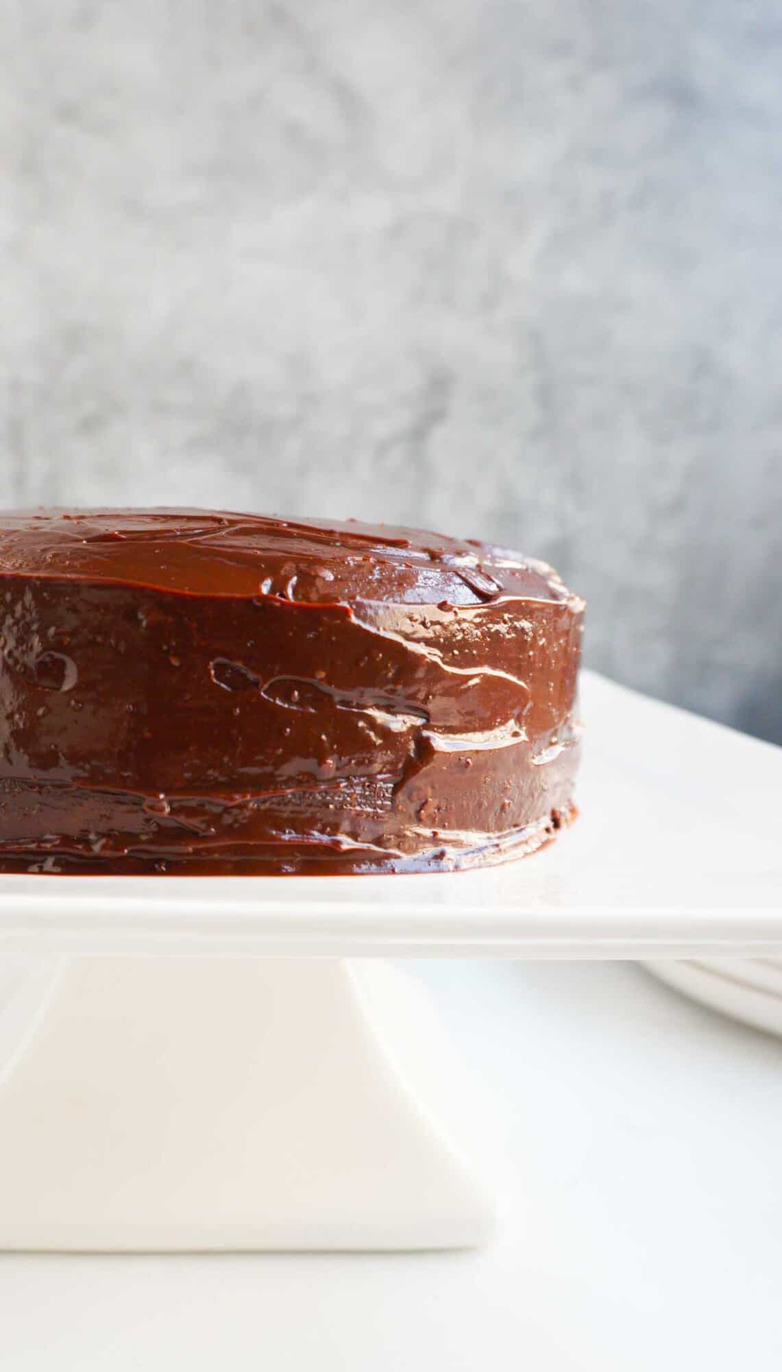 A frosted two layered almond flour chocolate cake on a white cake pedestal.