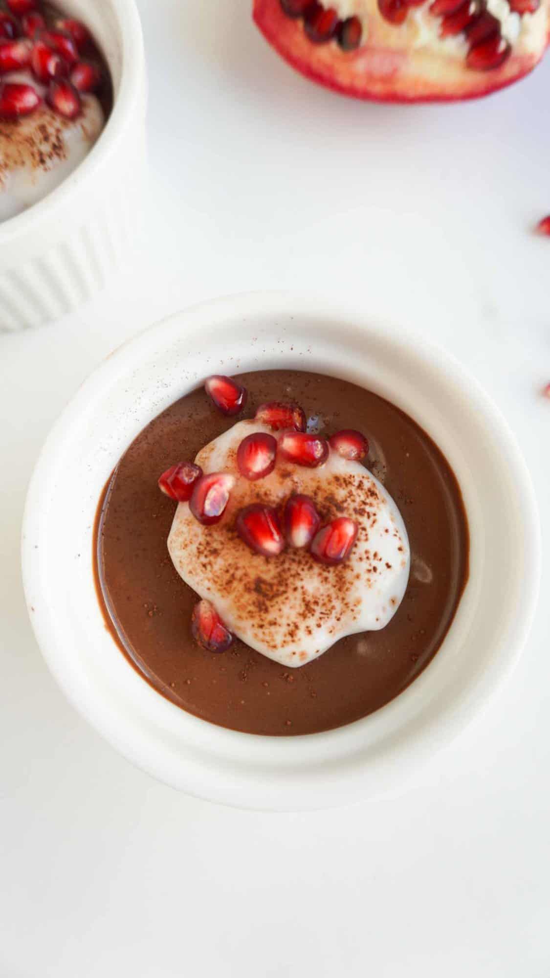 healthy vegan chocolate mousse in ramekin with coconut cream, cocoa powder  and pomegranate arils as garnish 