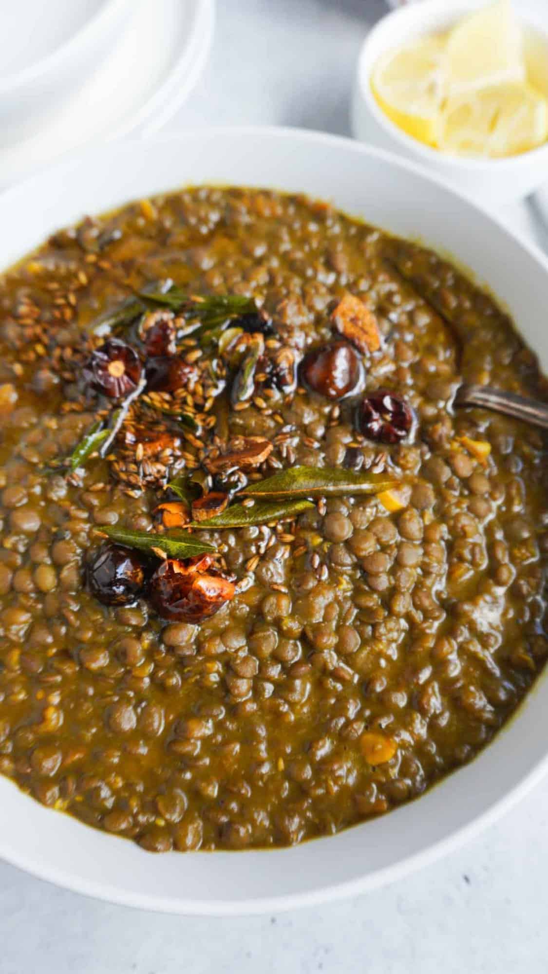 a bowl of kali masoor daal with tadka. Lemon wedges in background