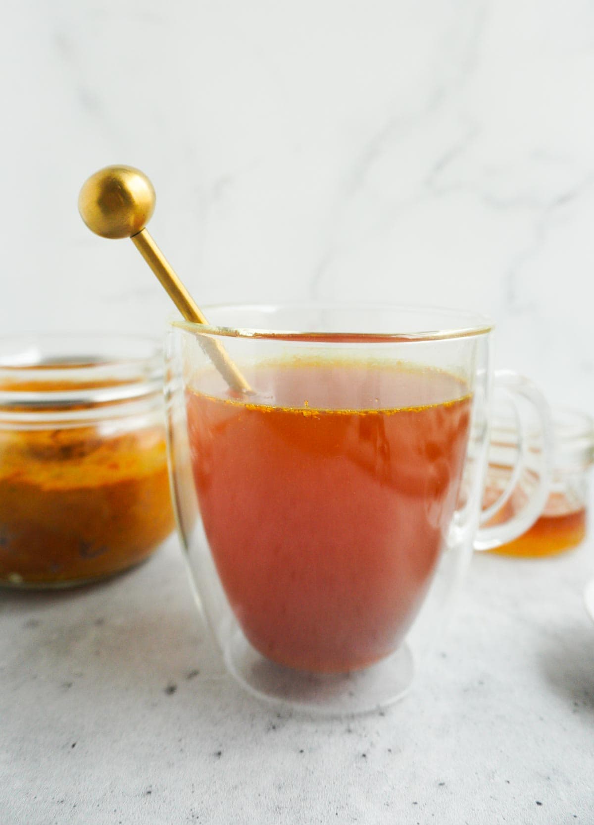 side view of turmeric paste in water with a jar of turmeric paste in the back