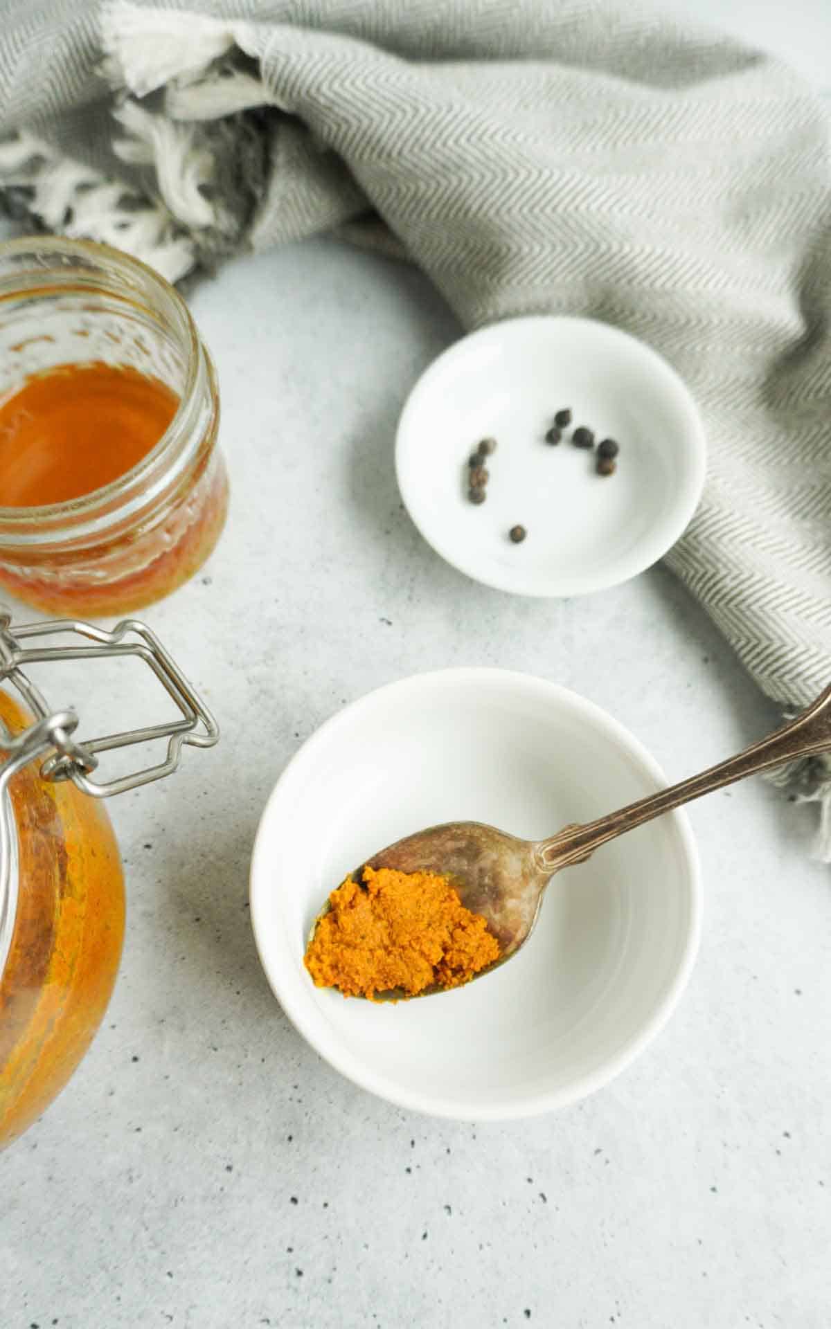 a spoon of turmeric paste with a jar in the back. A bottle of honey to the side