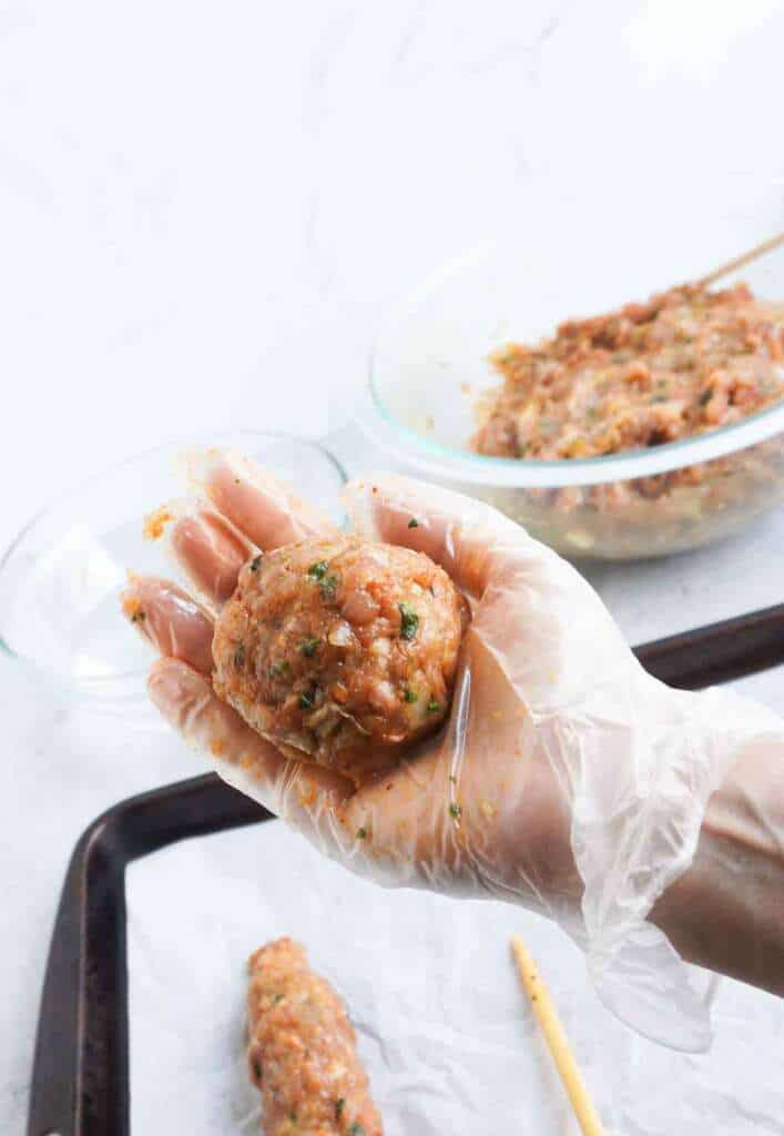 a gloved hand holding a ball of ground chicken