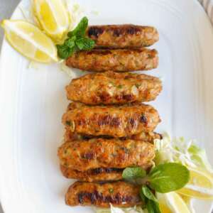 Chicken Seekh Kebabs on a platter with lemon wedges and mint garnish