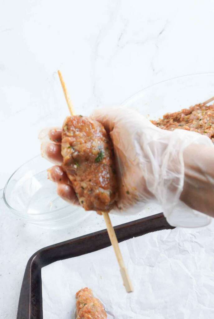 a hand shaping chicken seekh kebab on a chopstick