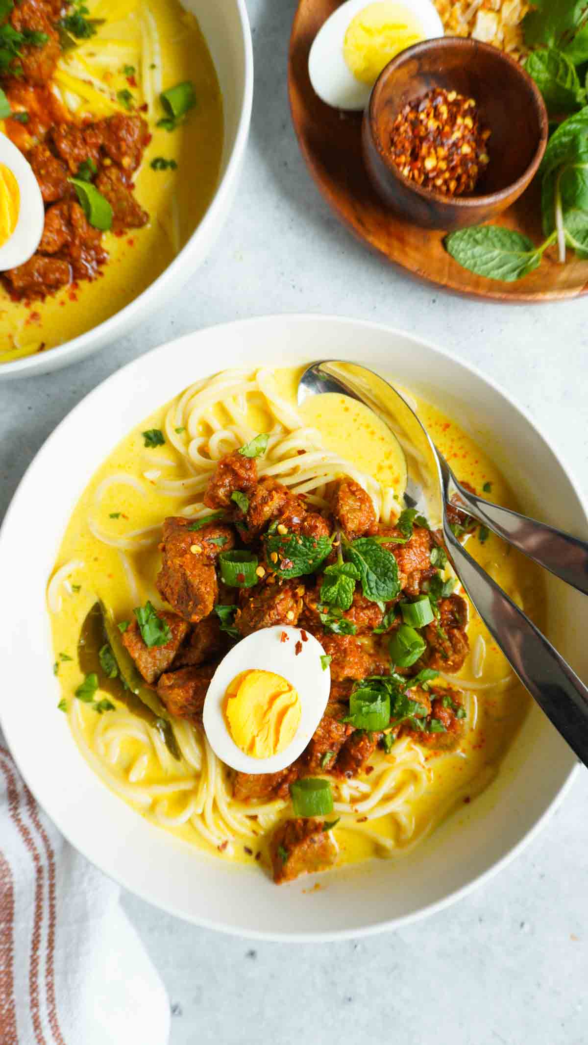 Beef khao suey in a bowl with a spoon and fork.