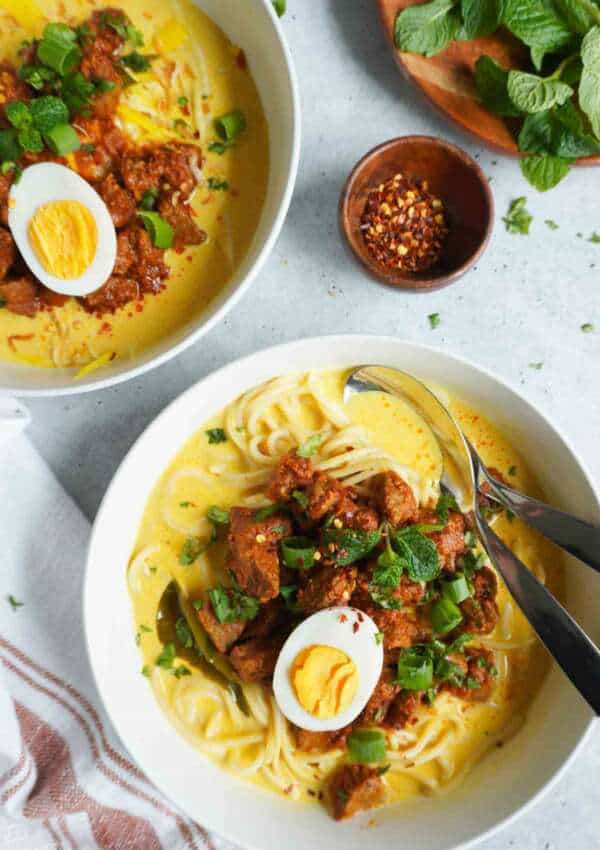 Beef Khao Suey in two bowls with crushed red pepper and mint garnish to the side