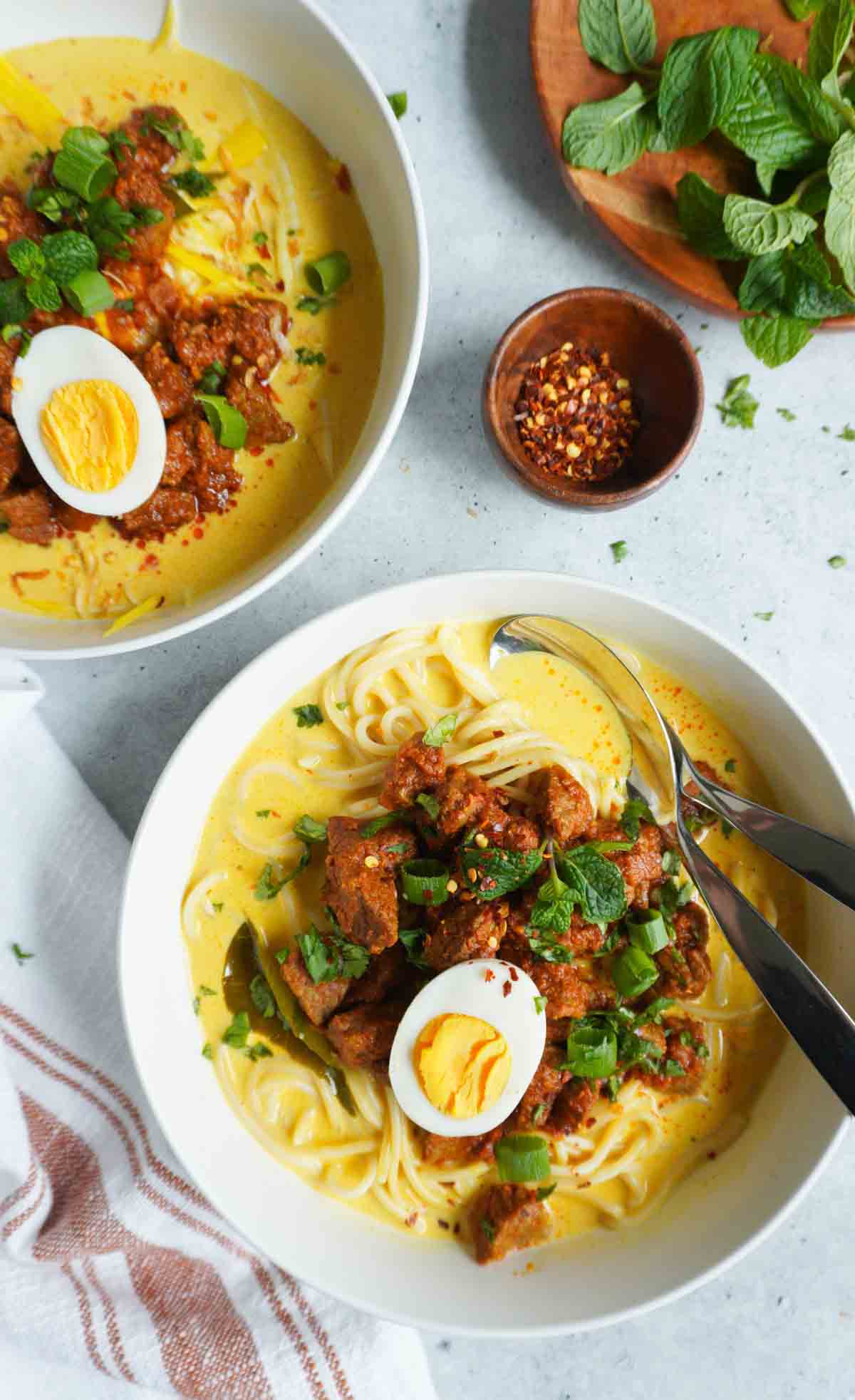 Beef Khao Suey in two bowls with crushed red pepper and mint garnish to the side