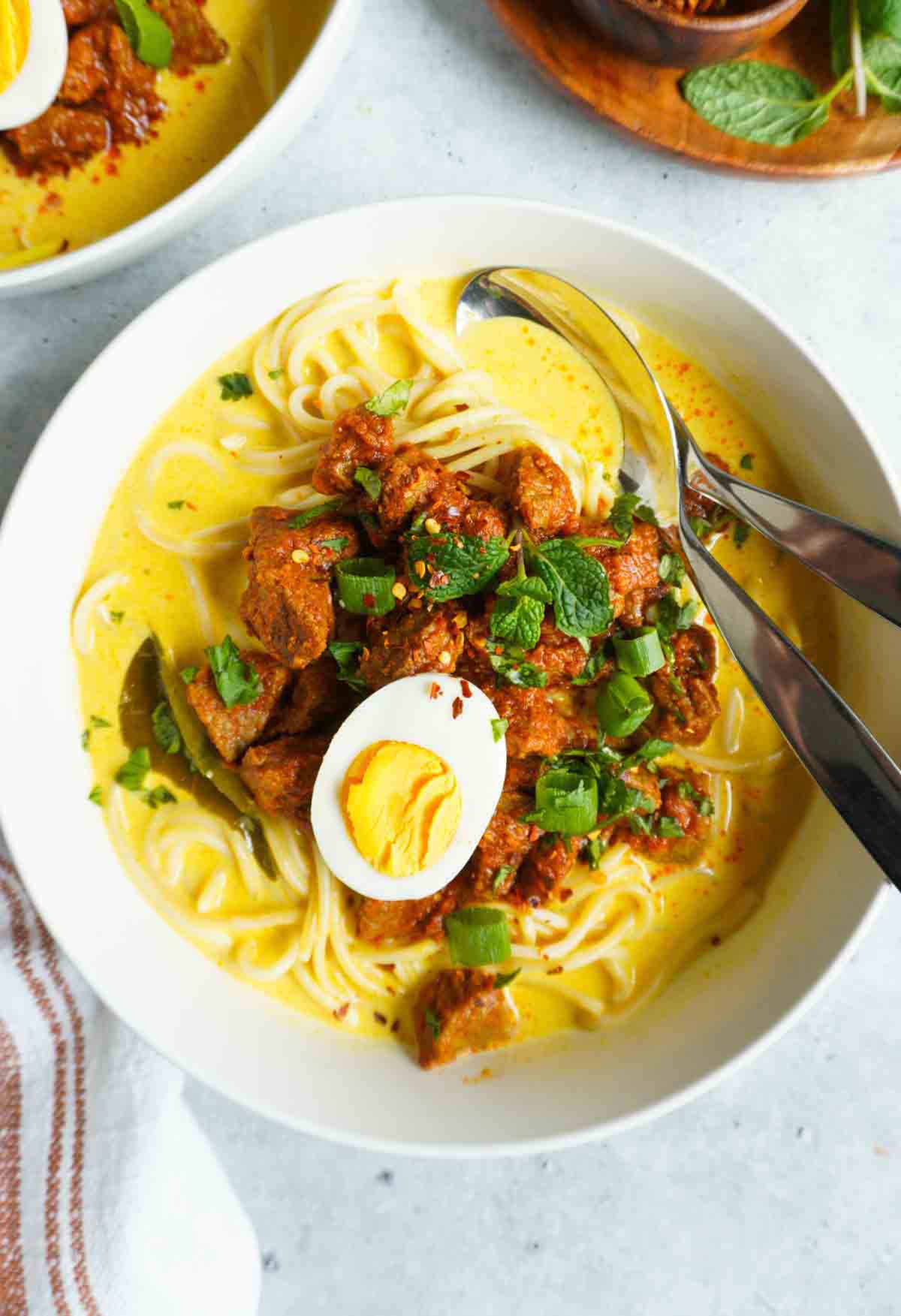 A bowl of beef khao suey in a bowl with another bowl to the top left