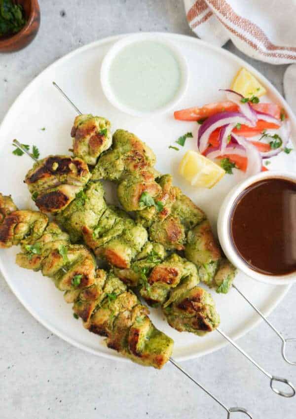 A platter with hara masala chicken tikka skewers with kachumbar and chutneys on the side