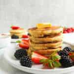 A stack of gluten free pancakes with a pat of butter on top. Berries on the plate.