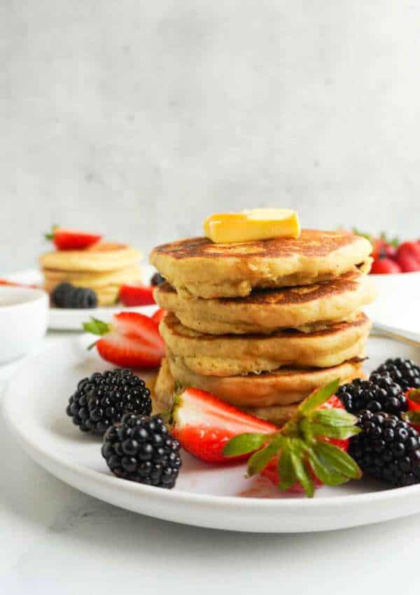 A stack of gluten free pancakes with a pat of butter on top. Berries on the plate.