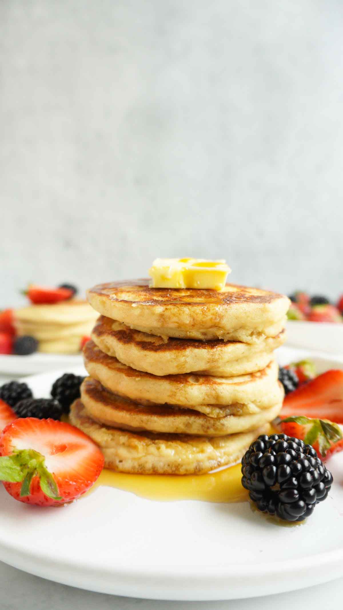 A stack of gluten-free buttermilk pancakes with berries around it and a pat of butter on top.
