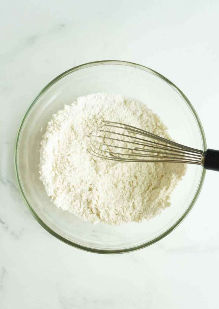 Dry ingredients for pancakes in a bowl with a whisk.