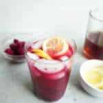 A glass of low sugar dragon fruit lemonade with another bowl of lemon and dragon fruit pieces and a pitcher of tea in the background