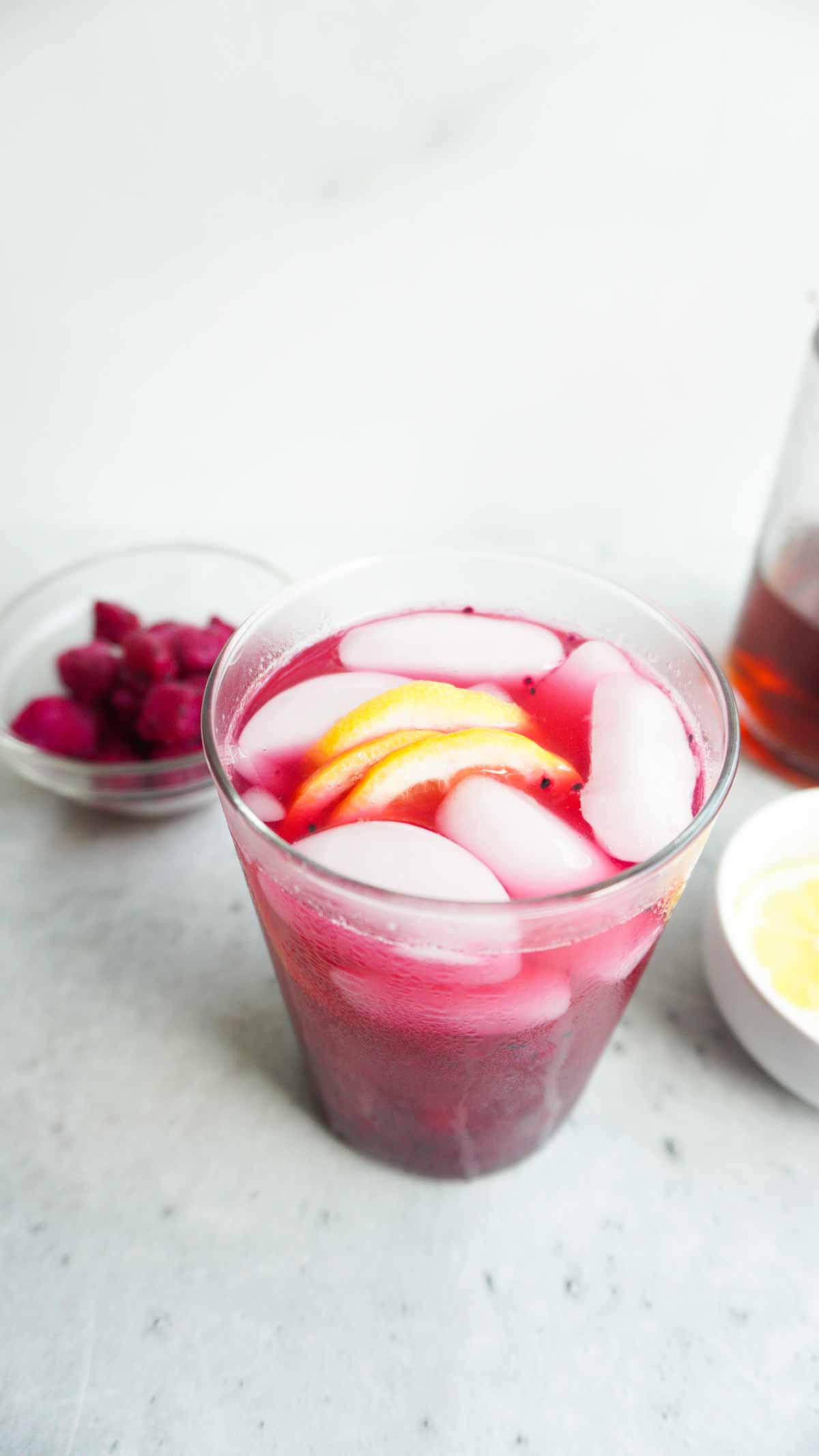 A glass with mango dragonfruit refresher and lemon slices. More dragon fruit chunks in the background. 