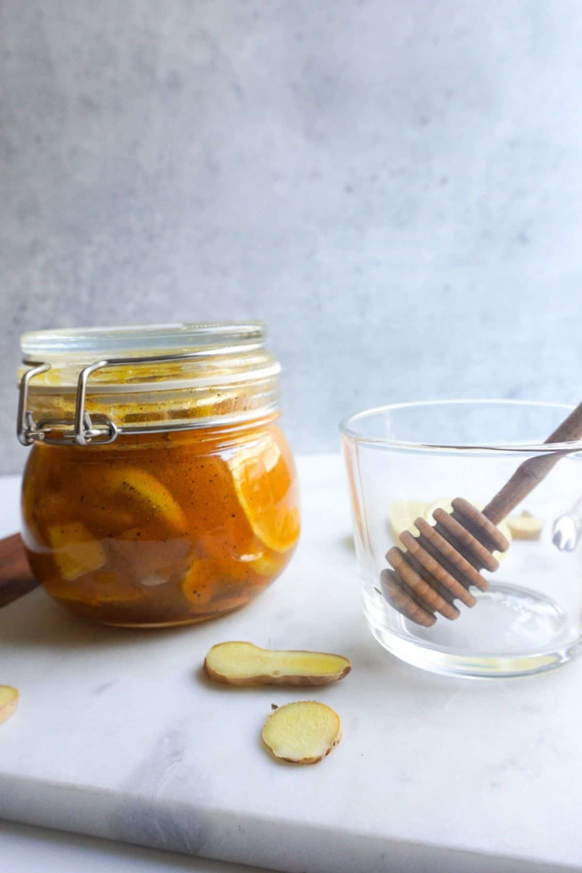 A clear jar of lemon ginger honey syrup on a white marble board.
