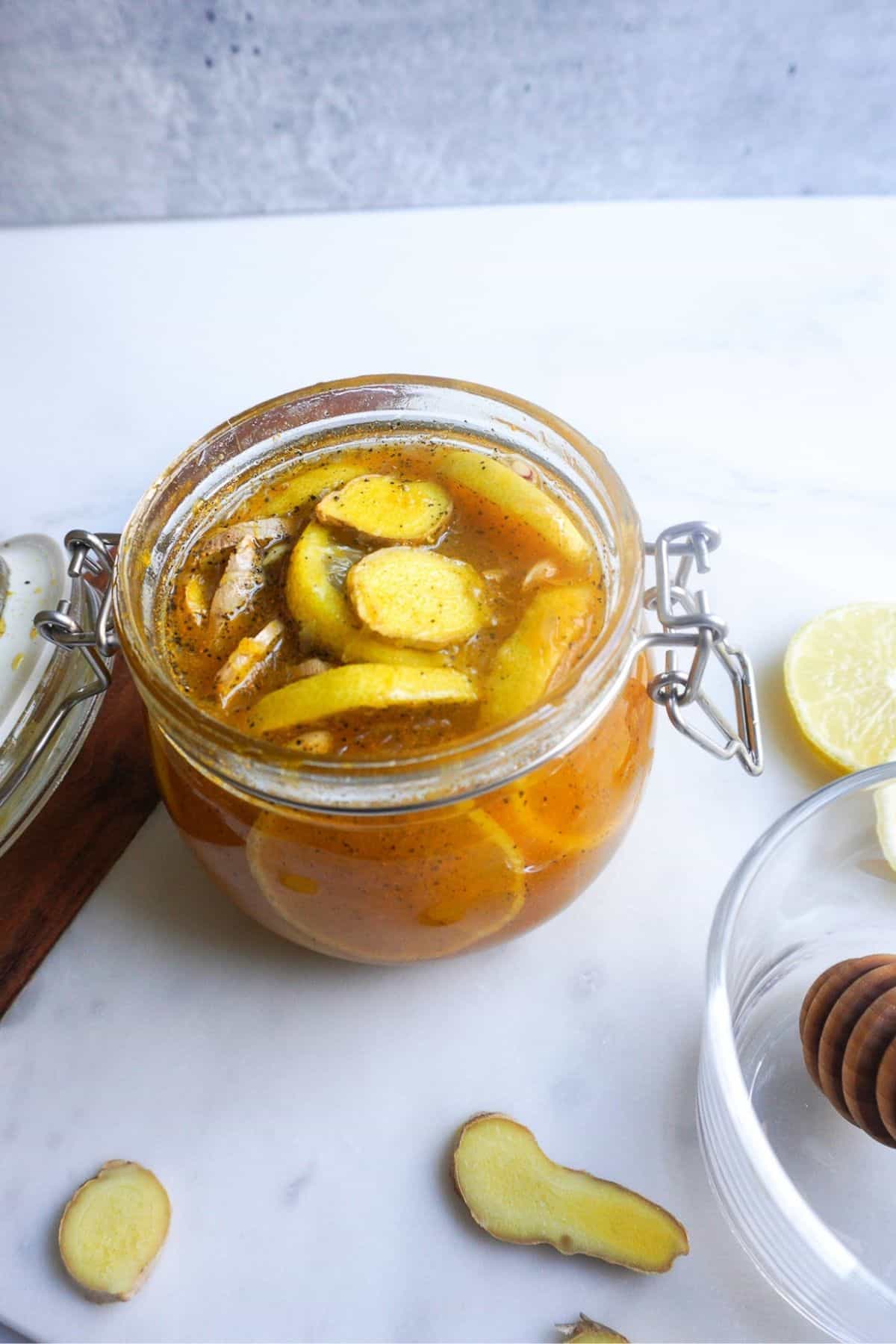 An open glass jar of lemon honey ginger syrup on a white marble cutting board.