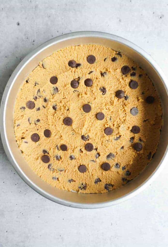 A cookie dough in a pan with chocolate chips.