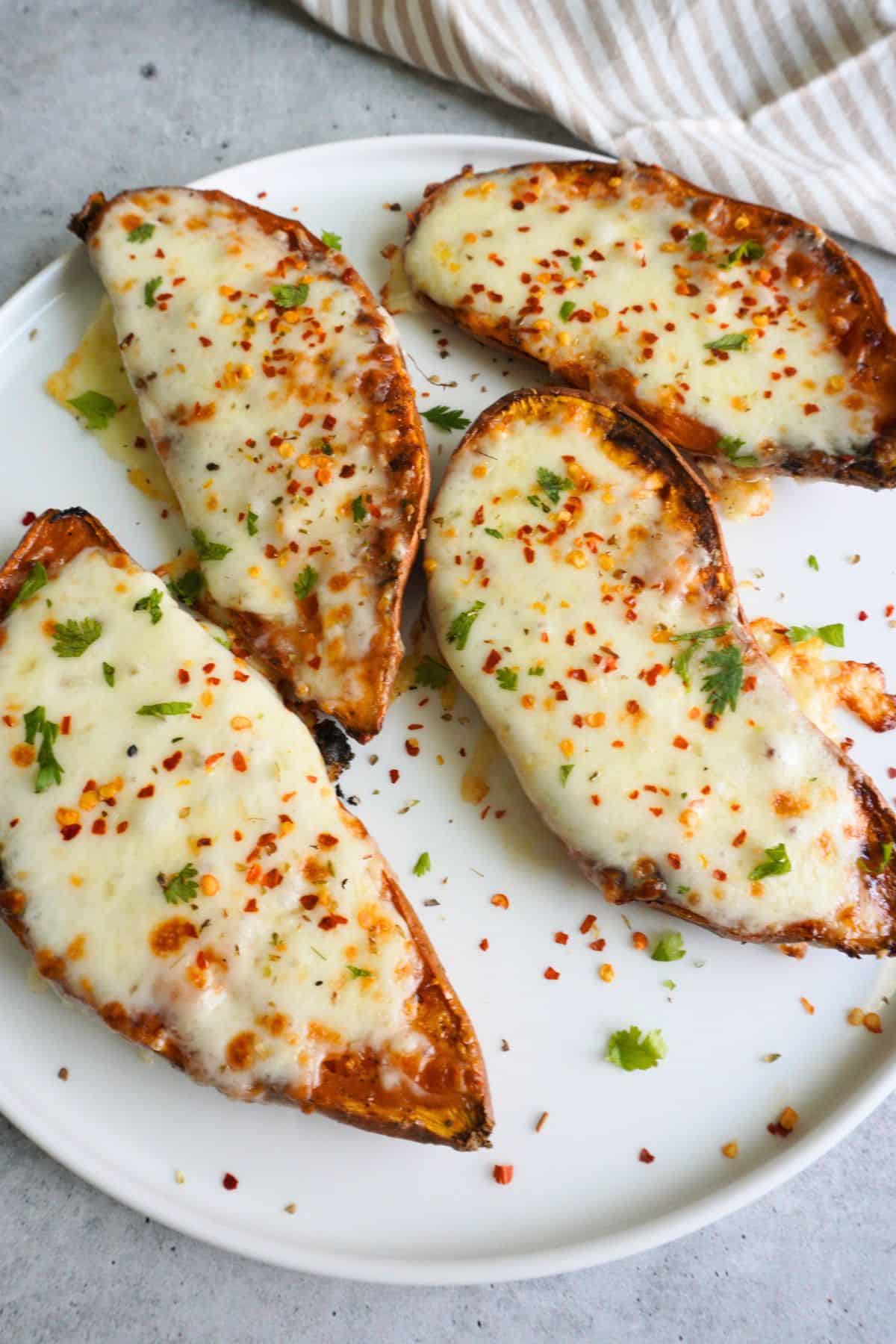 A white plate with cheese loaded sweet potato with crushed red pepper.