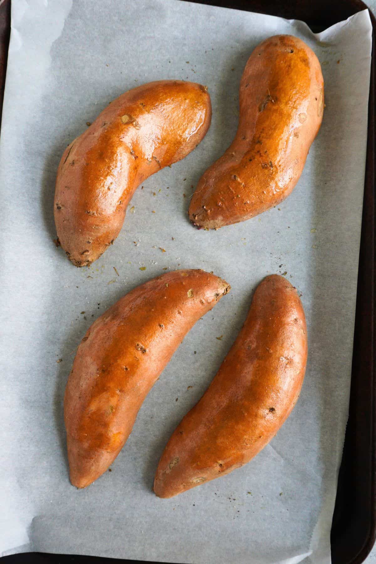 Sweet potato halves face down on a parchment-lined sheet pan.