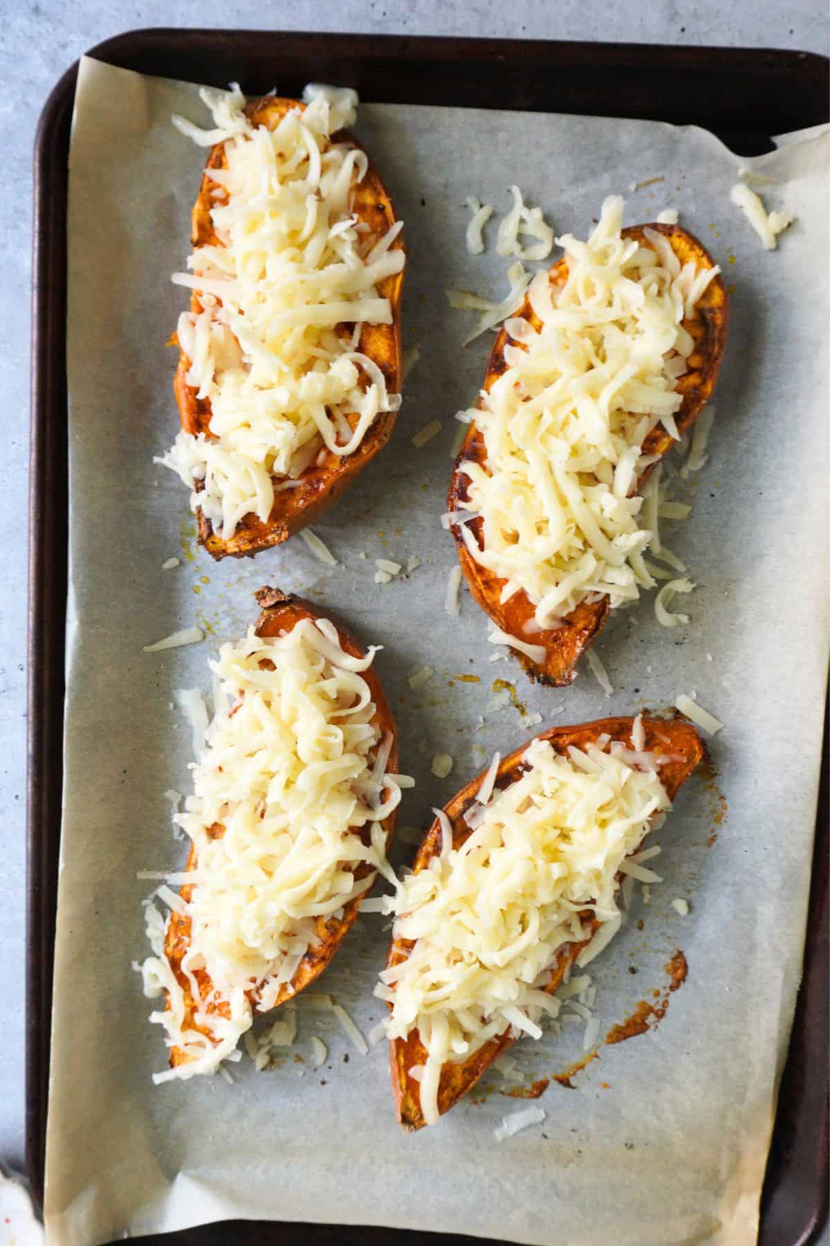 Mozzarella cheese on roasted sweet potato halves on a sheet pan.
