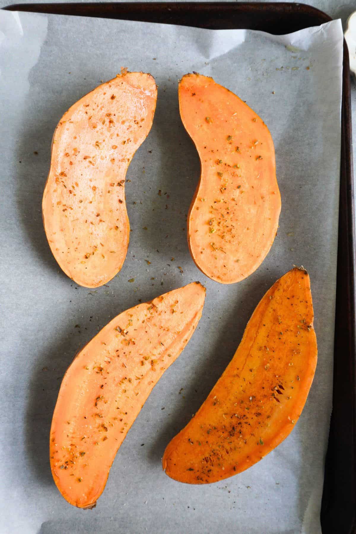 Sweet potato halves with oil and seasonings on a parchment-lined sheet pan.
