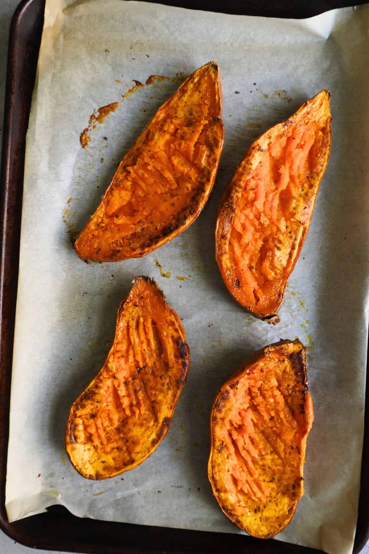 Roasted sweet potato halves on a parchment-lined sheet pan.