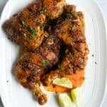 A white platter with chicken tikka thigh quarters with lime wedges.